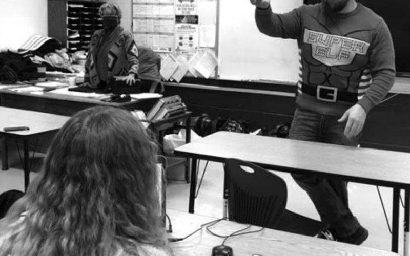 Teacher Ryan Gimbel, wearing his holiday sweater, addresses one of his high school classes.