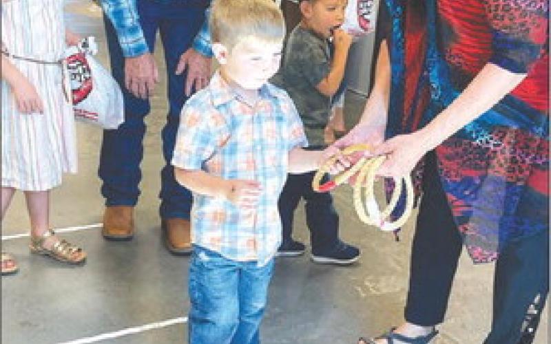 LOWER RIGHT: Canaan Parker learns how to do the ring toss with help from his sister Elyse, grandpa Bruce Parker, and game master Cindy Biegler. BEHIND is Asher Smith. Photos by Kathy Nelson