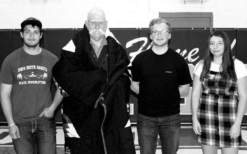 The DHS Powerlifting team recognized their coach, Shannon Hinrichs, by gifting him a star quilt. He is pictured with the 2024 senior powerlifters (L-R) Matthew Lemke, Case DePoy, and Nevaeh Farlee.