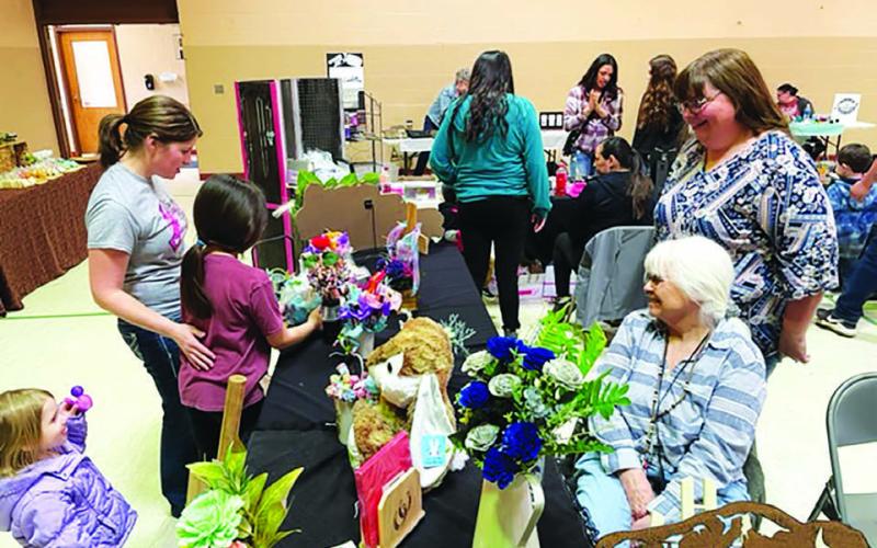 Melissa Herbel and Stella Brewer of the Rustic Rose in Eagle Butte displayed their wooden flower creations at the Timber Lake Craft Fair on Saturday, April 8. AT LEFT, Ali Eigelaar, who organized the Craft Fair, and her daughters, Thea and Leah, admire the merchandise.