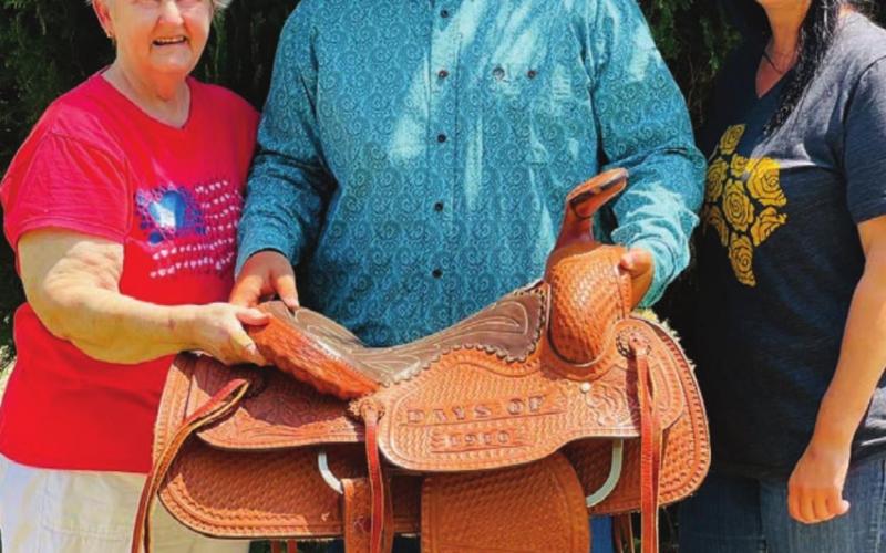 Carol Dellis (LEFT) with her daughter Sarah and 15-year-old grandson, Garrett, with the Days of 1910 saddle that Carol and her husband, Billy Bob Dellis, built in 1983. “It’s our legacy,” Carol said. “When it came I just hugged it. Just sitting here looking at it gives me such peace.”