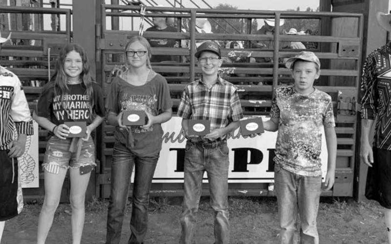 Winners of the calf scramble buckles at Sunday night’s Days of 1910 rodeo were L-R bull fighter Luke Henninger, Korbi Heck, Lexi Locken, Hudson Gill, Wyatt Sanderson and bull fighter Darwin Thompson. Photo by Robert Slocum