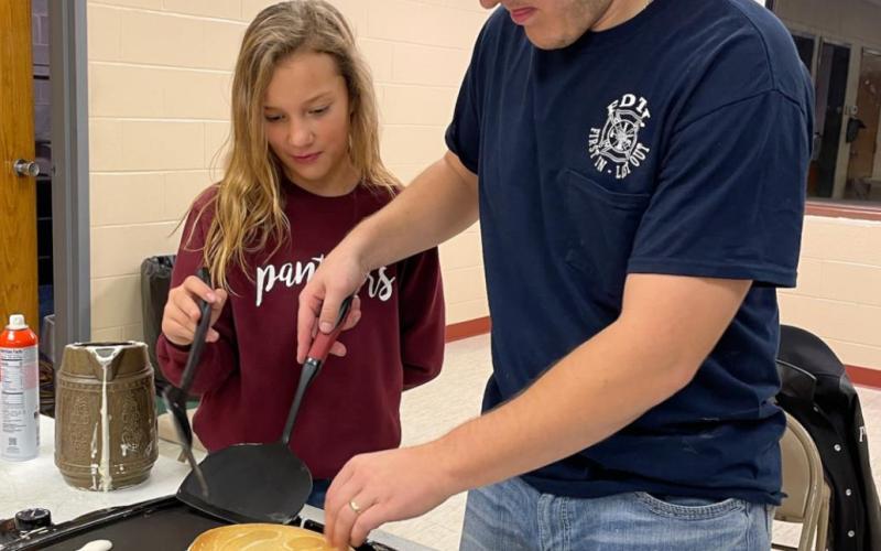 For more information contact Fireman Shaun Maher shows Pazlin Ducheneaux how to flip pancakes.