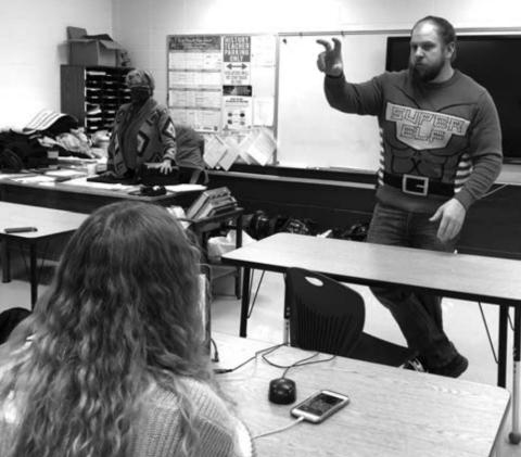 Teacher Ryan Gimbel, wearing his holiday sweater, addresses one of his high school classes.
