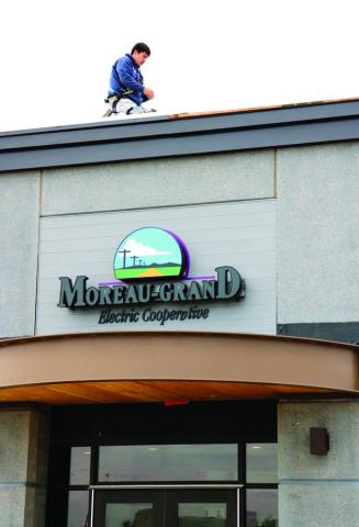 An electrical technician works atop the roof of the new Moreau-Grand Electric Cooperative building last week while wiring the sign above the main entrance. The sign looks most impressive when lit at night. Photo by Jon Flatland
