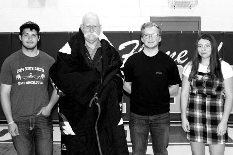 The DHS Powerlifting team recognized their coach, Shannon Hinrichs, by gifting him a star quilt. He is pictured with the 2024 senior powerlifters (L-R) Matthew Lemke, Case DePoy, and Nevaeh Farlee.