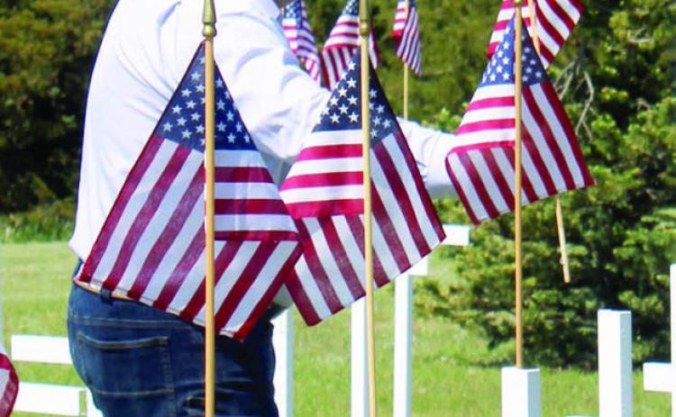 Ryan Maher places a flag on a cross marking a grave during the Memorial Day Program at Hillview Cemetery in Isabel. The placing of the flags is a tradition during the program. Photo by Patty Peacock.